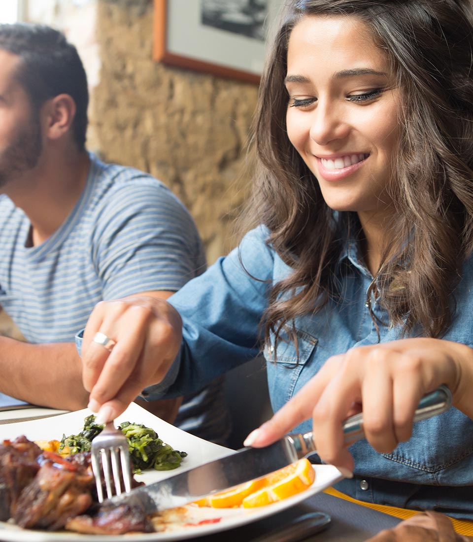 A young millennial woman enjoying a steak in a restaurant, with her friends.