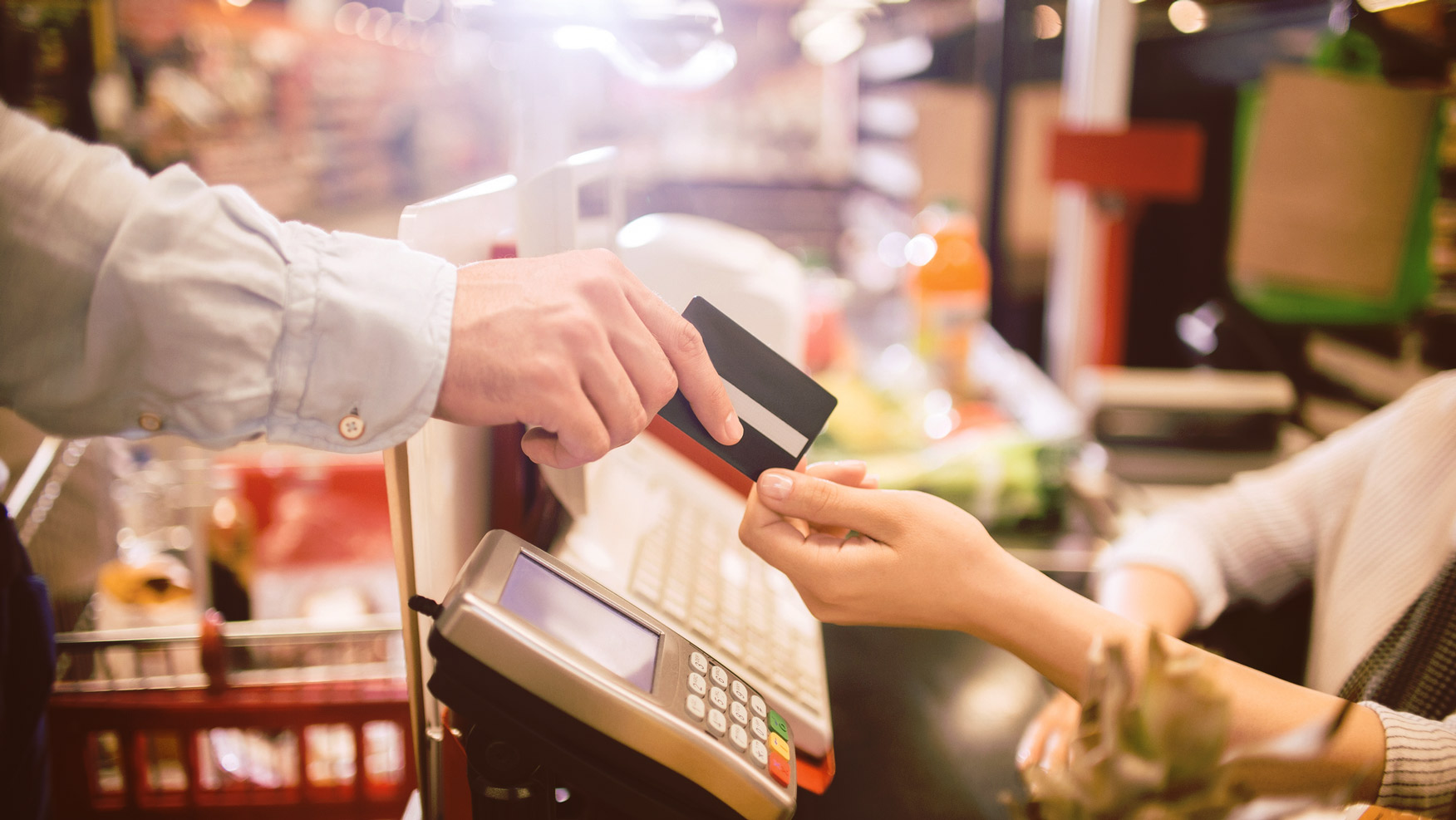 A grocery shopper hands a credit card to a grocery store cashier