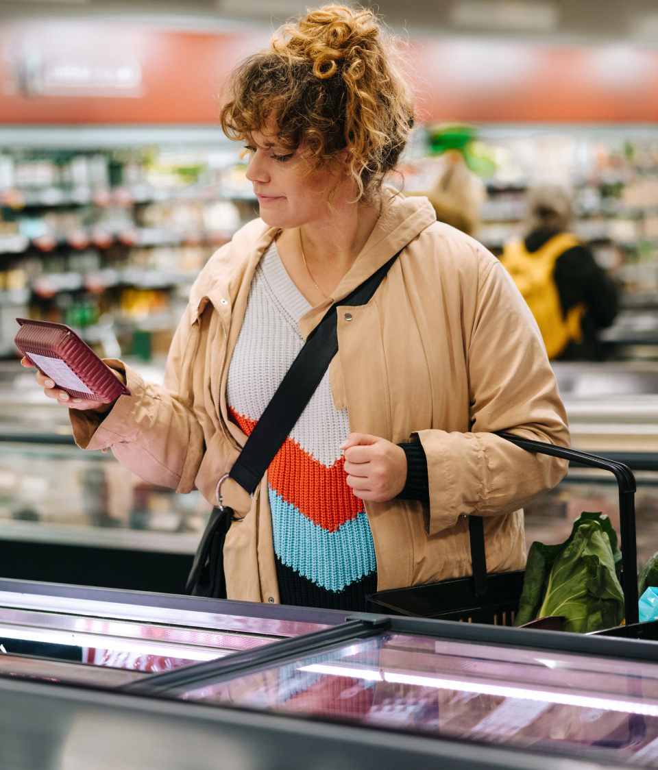 A woman shopping and looking at the labels on a meat package.