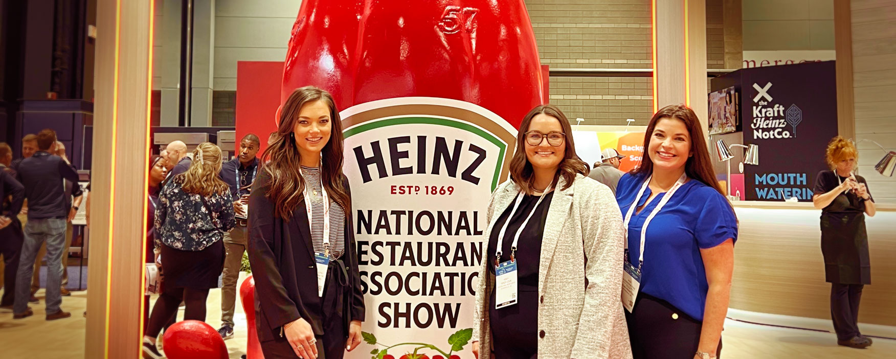 Three business women standing in front of a large Heinz ketchup display that says National Restaurant Association Show