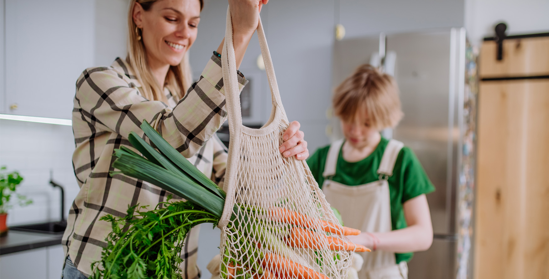 Woman holding vegetables in a mesh bag in a kitchen with her child