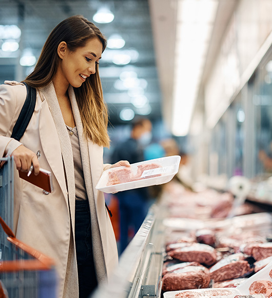 woman reading an on-pack label at a meat case