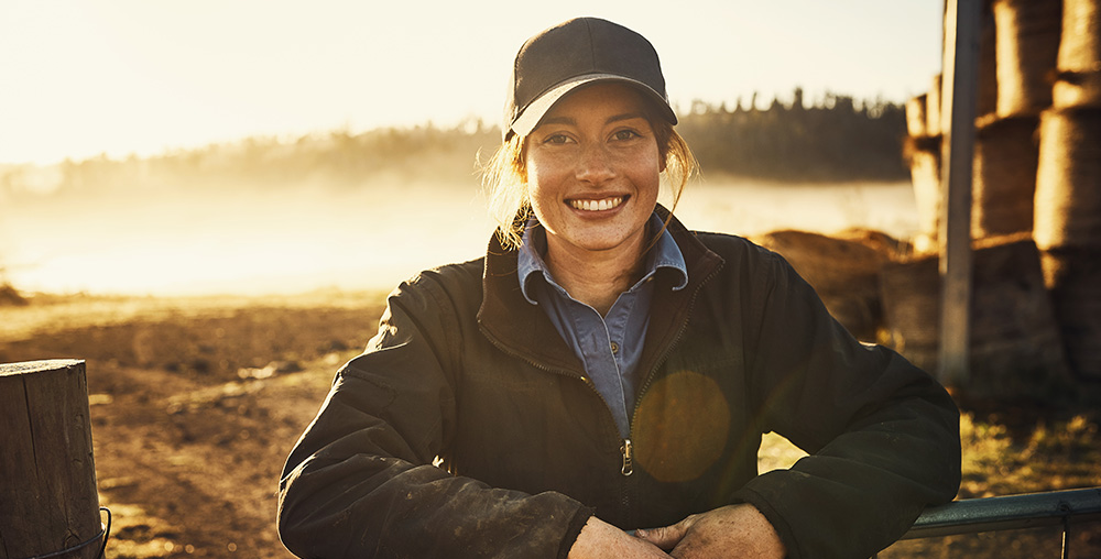 Smiling woman wearing a hat standing by a gate in a field